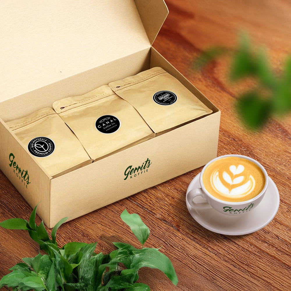 Organic koffie proefpakket met drie zakjes in een doos, een kopje cappuccino en groene blaadjes op houten tafel