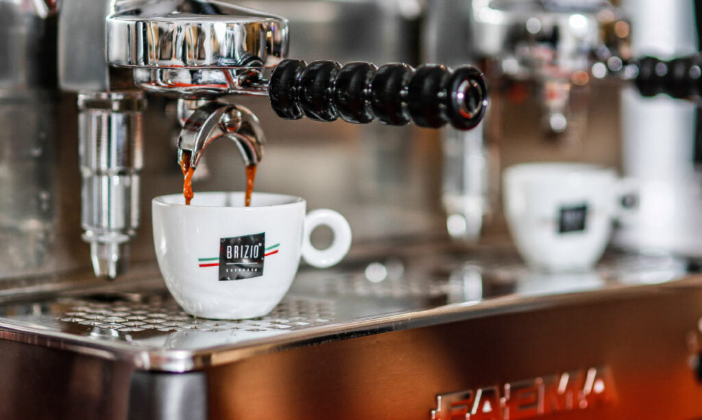 Een close-up van een espressomachine die verse espresso schenkt in een wit Brizio kopje, met een tweede kopje op de achtergrond.